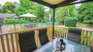 A covered outdoor seating area with a glass table and chairs, surrounded by a metal fence and greenery. - SILVER BIRCHES HOLIDAY VILLAGE - UNIT 9 (Bright)