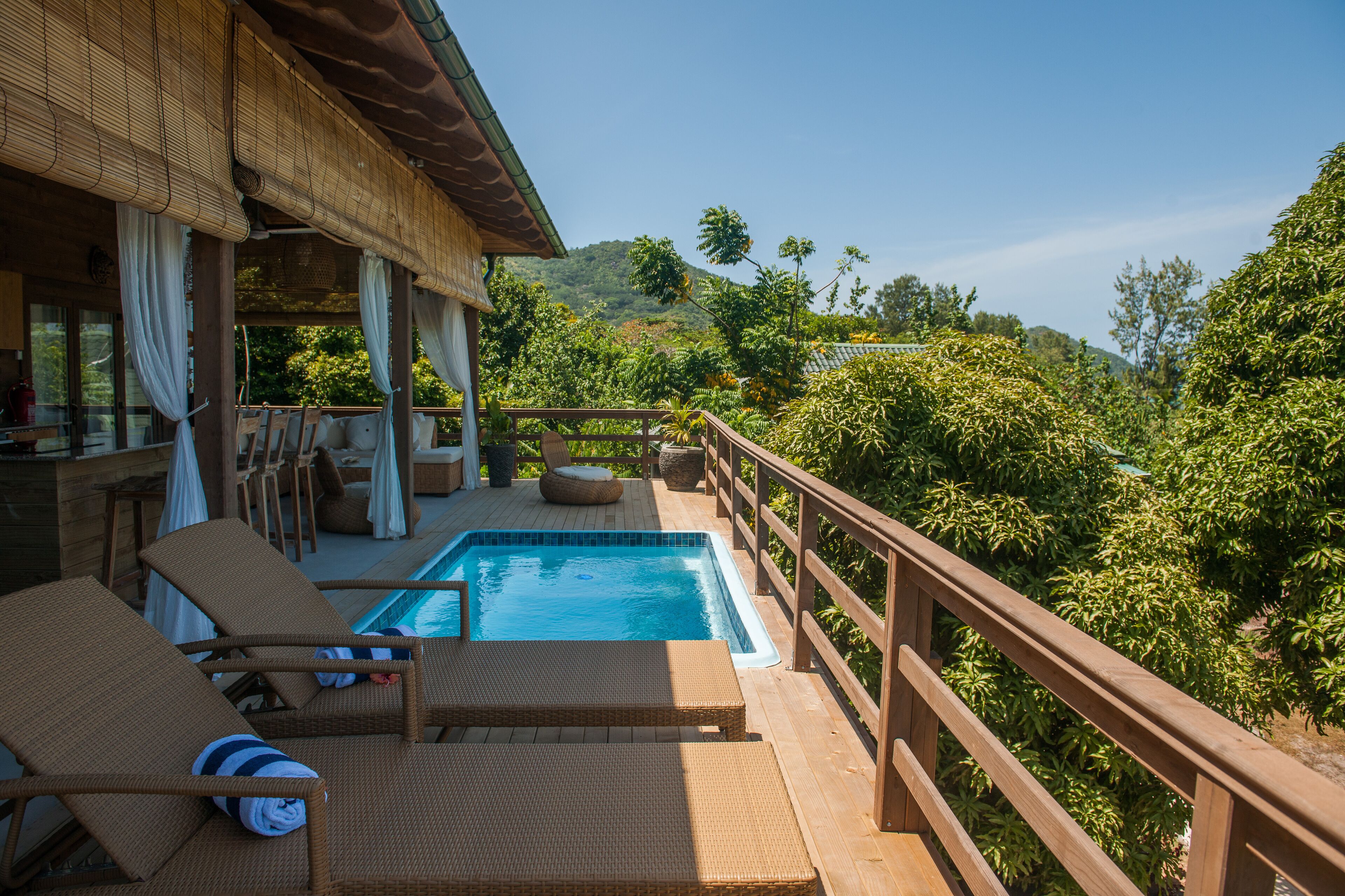 A poolside area with lounge chairs and a wooden deck overlooking lush greenery.