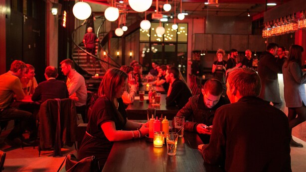 A crowded bar with people sitting at tables, a staircase in the background, and hanging spherical light fixtures. - Providing Stylish City Living within the vibrant shore area (Edinburgh)