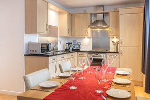 A modern kitchen with wooden cabinets, stainless steel appliances, and a dining table set for six with wine glasses.