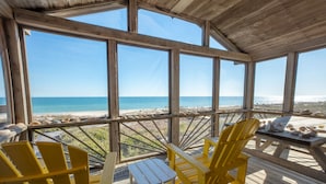 A covered outdoor area with wooden flooring, yellow Adirondack chairs, and a table with seashells. - Beachfront, Plantation, Pet Friendly (Eastpoint)