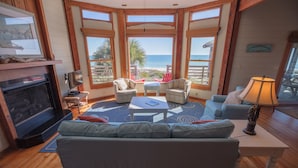 A spacious living room with a large window overlooking the beach, a fireplace, and a comfortable seating area with a sofa and chairs. - Beachfront, Plantation, Pet Friendly (Eastpoint)