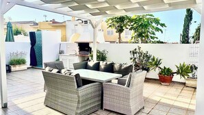 Eine Terrasse im Freien mit Korbmöbeln, einem Grill und Topfpflanzen.