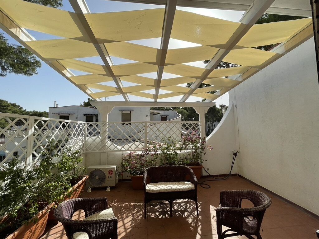 A covered patio area with wicker furniture, potted plants, and a white lattice fence.