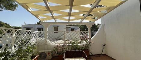 A covered patio area with wicker furniture, potted plants, and a white lattice fence.