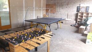 Una habitación con mesa de futbolín, mesa de ping pong y dardos.