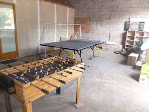 A room with a foosball table, ping pong table, and dartboards.