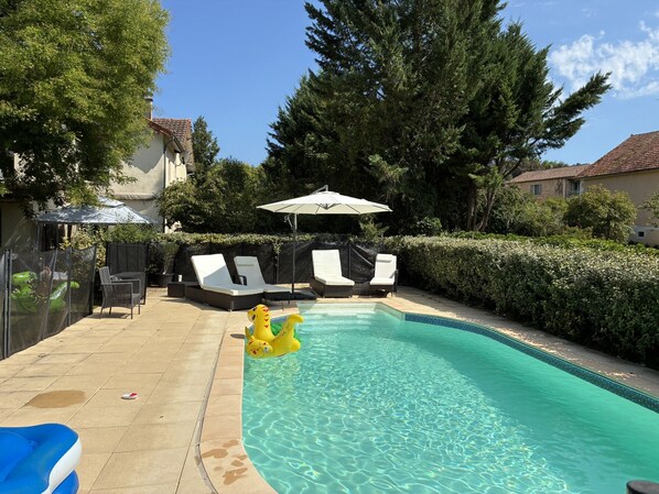 A swimming pool with lounge chairs and a sun umbrella, surrounded by trees and a fence.