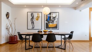 Uma área de refeições com mesa de madeira, cadeiras pretas e dois quadros na parede.