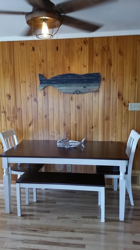 Un comedor con pared de madera, ventilador de techo y una mesa con sillas.