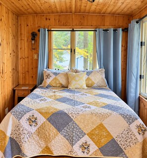 A wooden cabin bedroom with a large bed, a nightstand, and a window with curtains.