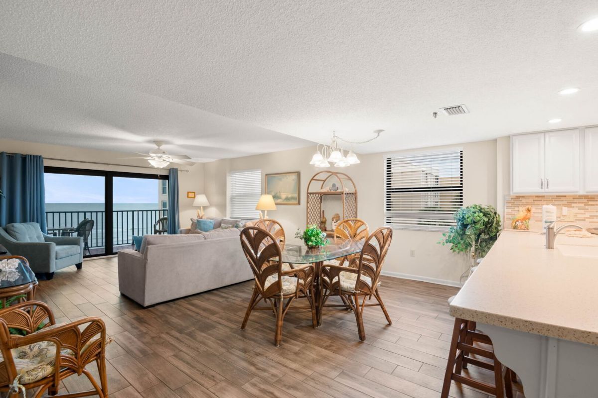 A modern living room with a glass dining table, wicker chairs, a sofa, and a balcony with a view.