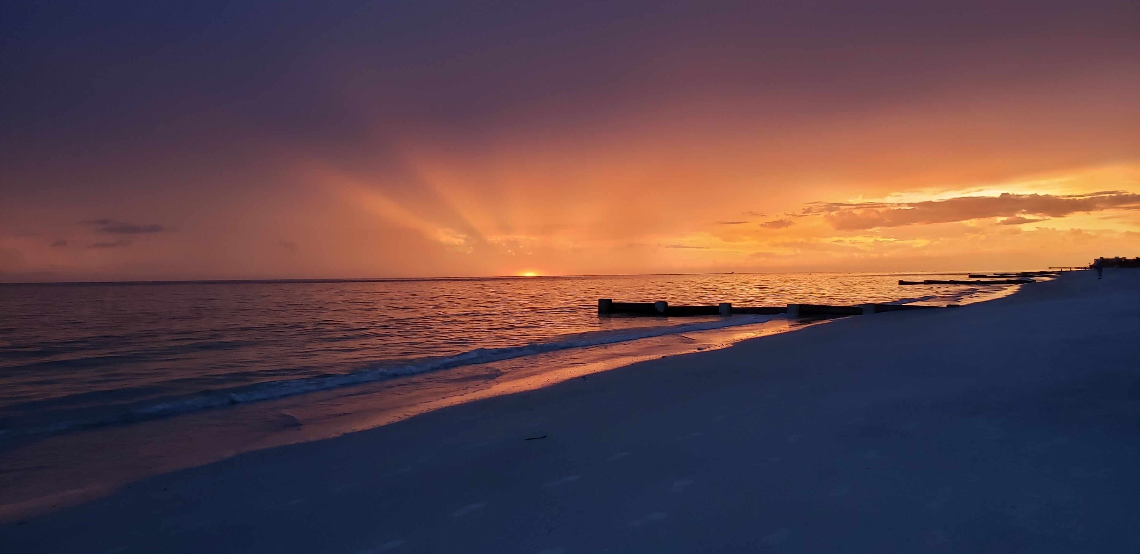 A beach scene with a sunset, calm sea, and a pier extending into the water.