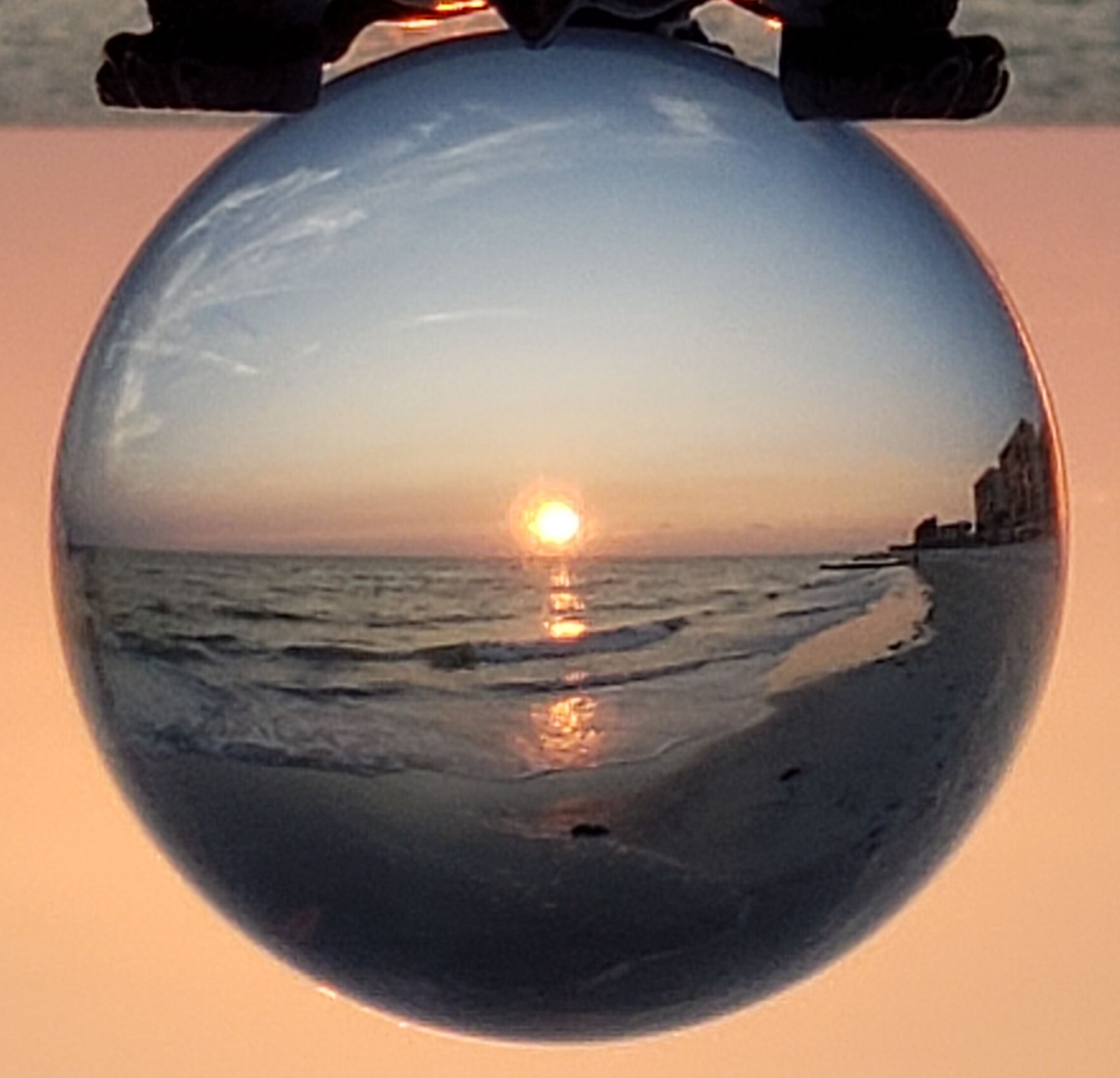 Escena de platja amb el sol ponent-se sobre l'oceà, vista a través d'una esfera.