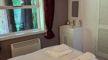 A hotel room with a bed, a window with a view of trees, a radiator, a mirror, and a cabinet.