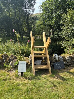 A wooden bench in a natural setting with signs indicating 'Woodland Walk'. - Cosy Log Cabin Near Loch Earn (Lochearnhead, Stirlingshire)