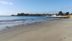 A beach with a clear sky, calm sea, and a distant shoreline with buildings. - Vue mer panoramique, spa de luxe, proche plage, l'un des Gîtes de Fabie (Plougonvelin)