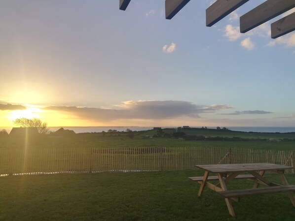 A wooden picnic table in a grassy area with a view of the sunset over a distant landscape.