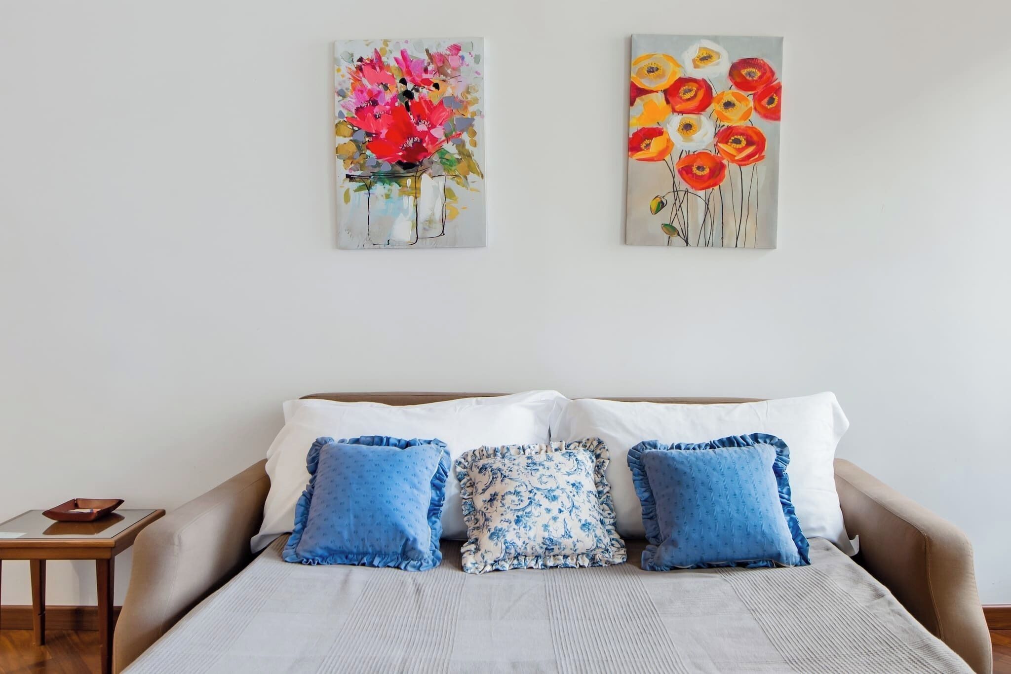 A bedroom with a bed, pillows, and two paintings on the wall.