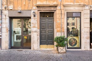 A building facade with a large glass window, a dark wooden door, and a small potted plant. - Piazza Navona-Coronari House (Roma)