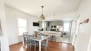 A modern kitchen with a dining area, featuring a central island, built-in appliances, and a large window. - Sweet  Victorian Beach Cottage (Cape Charles)