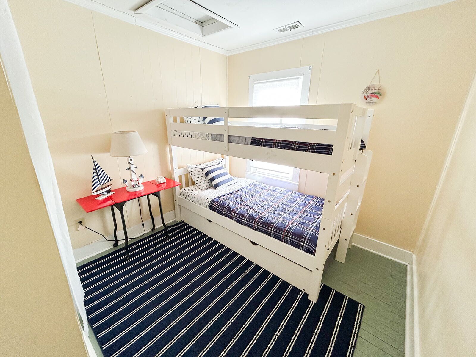Een slaapkamer met een stapelbed, een rode bureau, een lamp en een gestreept vloerkleed.