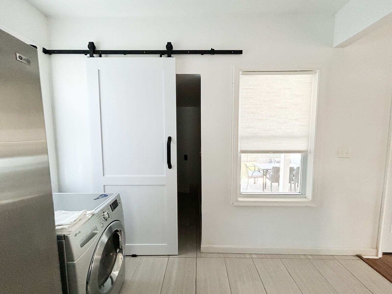 A laundry room with a washing machine, a sliding door, and a window with blinds.