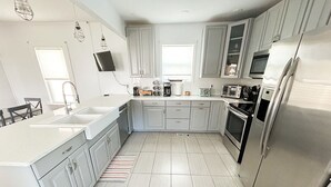 A modern kitchen with white cabinets, stainless steel appliances, and a large island. - Sweet  Victorian Beach Cottage (Cape Charles)