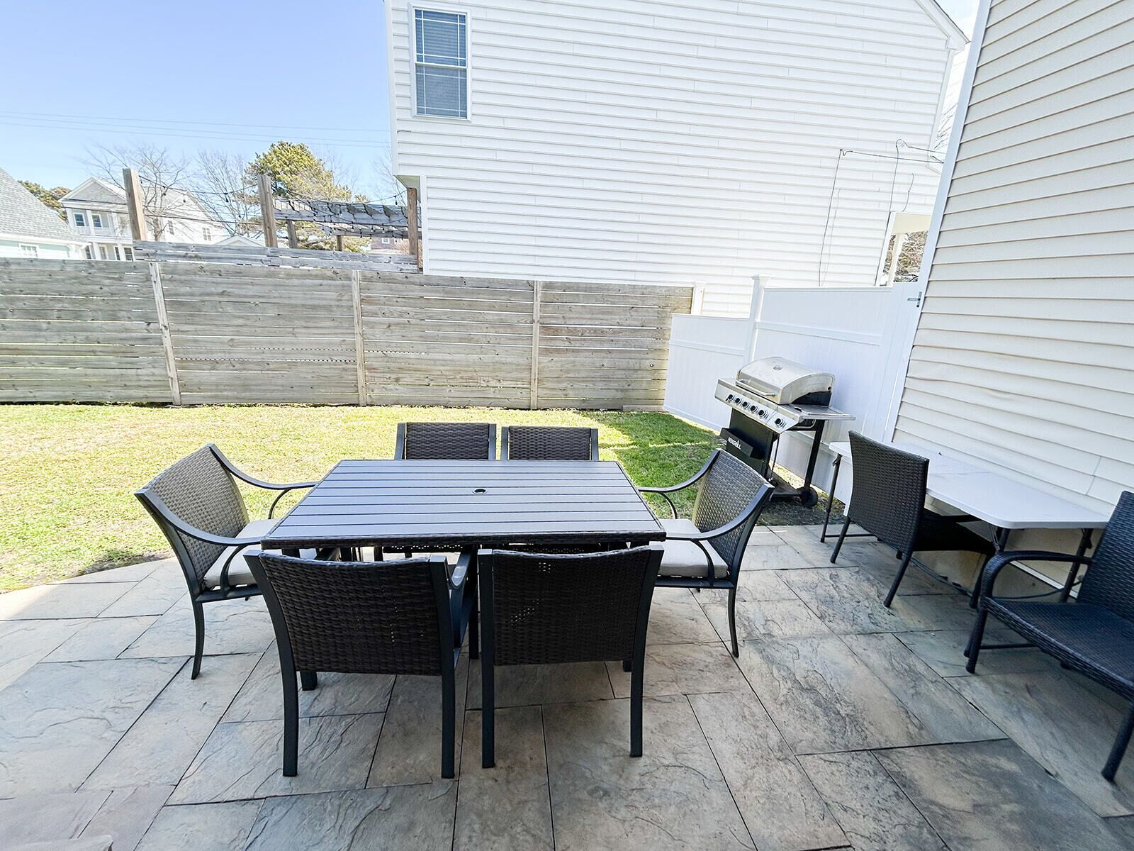 An outdoor patio with a table and chairs, a grill, and a wooden fence.