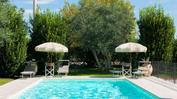 A swimming pool with two umbrellas and lounge chairs. - "Casale Giacinta" ancient cottage between sea and mountains with swimming pool (Pianella (PE))