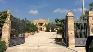 A gated entrance to a property with a paved driveway leading to a building with a tiled roof. - "Casale Giacinta" ancient cottage between sea and mountains with swimming pool (Pianella (PE))