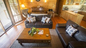 Ein gemütliches Wohnzimmer mit Holzboden, einer schwarzen Ledersofa, einem Holztisch und einer Essecke mit Küchenzeile.