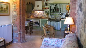 A rustic kitchen with exposed brick walls, a dining area with a table and chairs, and a sofa in the foreground. - Francesca 3 Extra Suite pool and whirlpool (Camaiore)