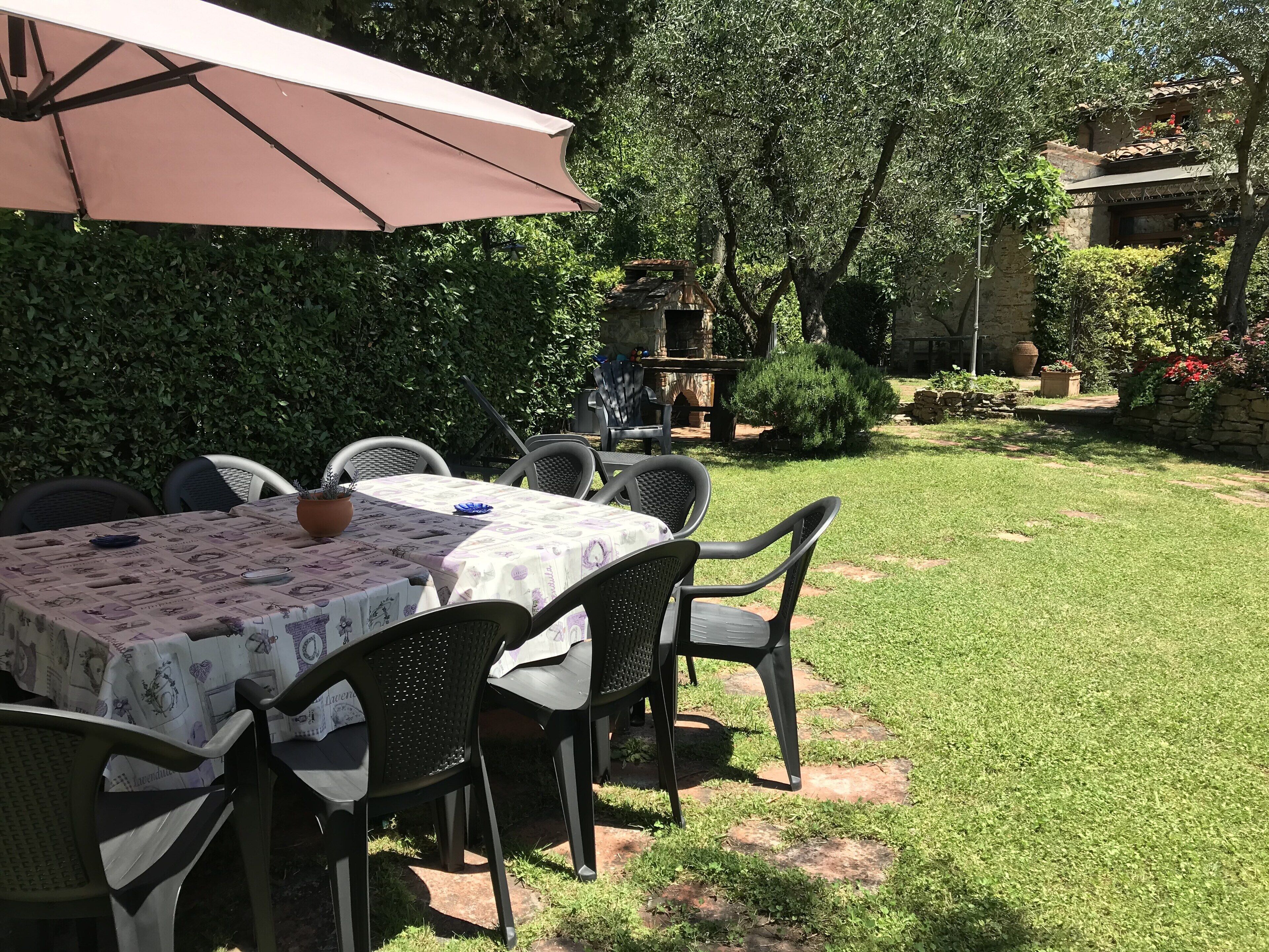 An outdoor patio with a table set for dining, surrounded by chairs, and a large umbrella providing shade.