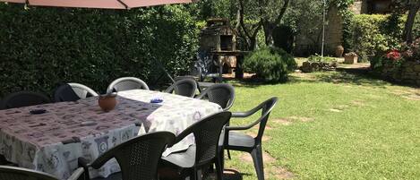 An outdoor patio with a table set for dining, surrounded by chairs, and a large umbrella providing shade.