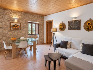 A cozy living area with a stone wall, a dining table with chairs, a sofa, and a floor lamp. - Quinta Do Pomarinho 46328/AL  (Tavira)