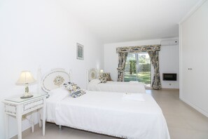 Une chambre avec deux lits, une table de chevet avec une lampe, une télévision et une vue sur un jardin, visible à travers une fenêtre avec des rideaux.