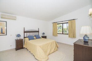 Une chambre à coucher comprenant un lit, une table de chevet, une commode, une fenêtre avec des rideaux et une lampe fixée au mur.