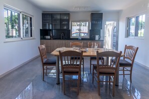 Un coin repas avec une table ronde, six chaises en bois et une cuisine en arrière-plan.
