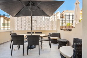 Een terras met een tafel, stoelen, een grote parasol en een sierhekwerk.