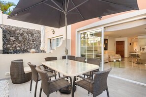 A dining area with a glass table and wicker chairs, a stone wall, and a large umbrella. - residential apartment in the Paraiso del Palm-mar  (Palm-Mar)