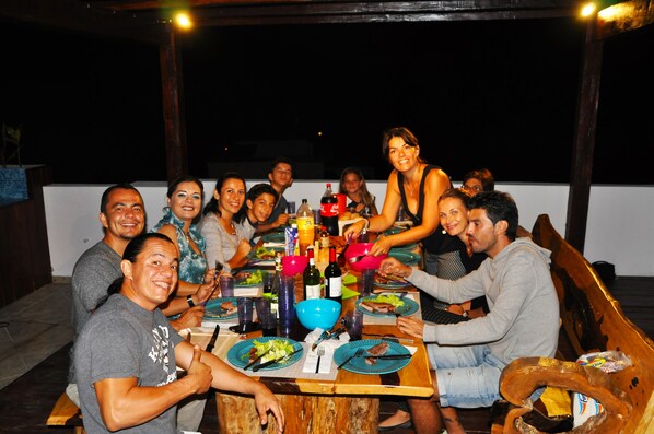 A group of people dining at an outdoor table with various dishes, drinks, and bottles.