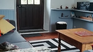 Un salon avec un canapé, une table en bois et un coin cuisine équipé d’une radio et d’étagères.