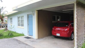 Une maison de plain-pied avec une porte bleue et un garage. Une voiture rouge est garée à l’intérieur du garage.