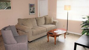 Un salon avec un canapé beige, un fauteuil gris, une table basse en bois et un lampadaire.