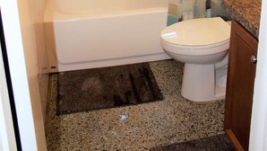 Une salle de bain avec douche, toilettes et une fenêtre équipée de stores.