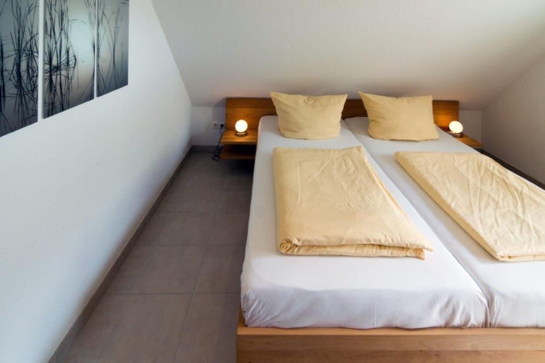 A small, single-bed room with a wooden headboard, two bedside tables with lamps, and a large abstract painting on the wall.