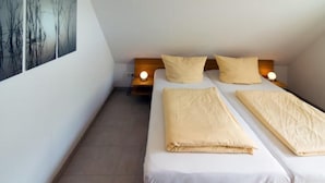 Una habitación pequeña con cama individual, cabecera de madera, dos mesitas de noche con lámparas y un cuadro abstracto grande en la pared.