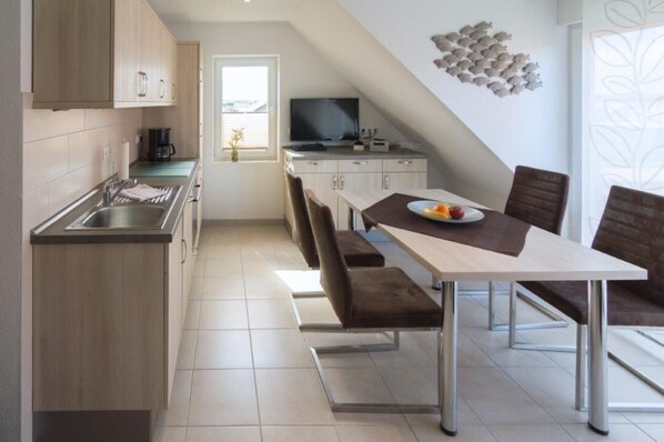 A modern kitchen with a dining area, featuring a TV, a coffee machine, and a decorative wall piece. - Vacation apartment Strandlilie (Norddeich)