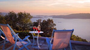 Eine Terrasse mit zwei Stühlen und einem Tisch, mit Blick auf ein Gewässer und die Ferne.
